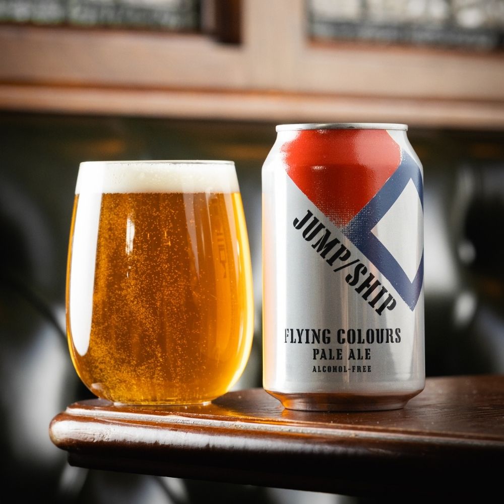 Can of Jump/Ship Flying Colours Pale Ale next to a glass of beer on a wooden surface.