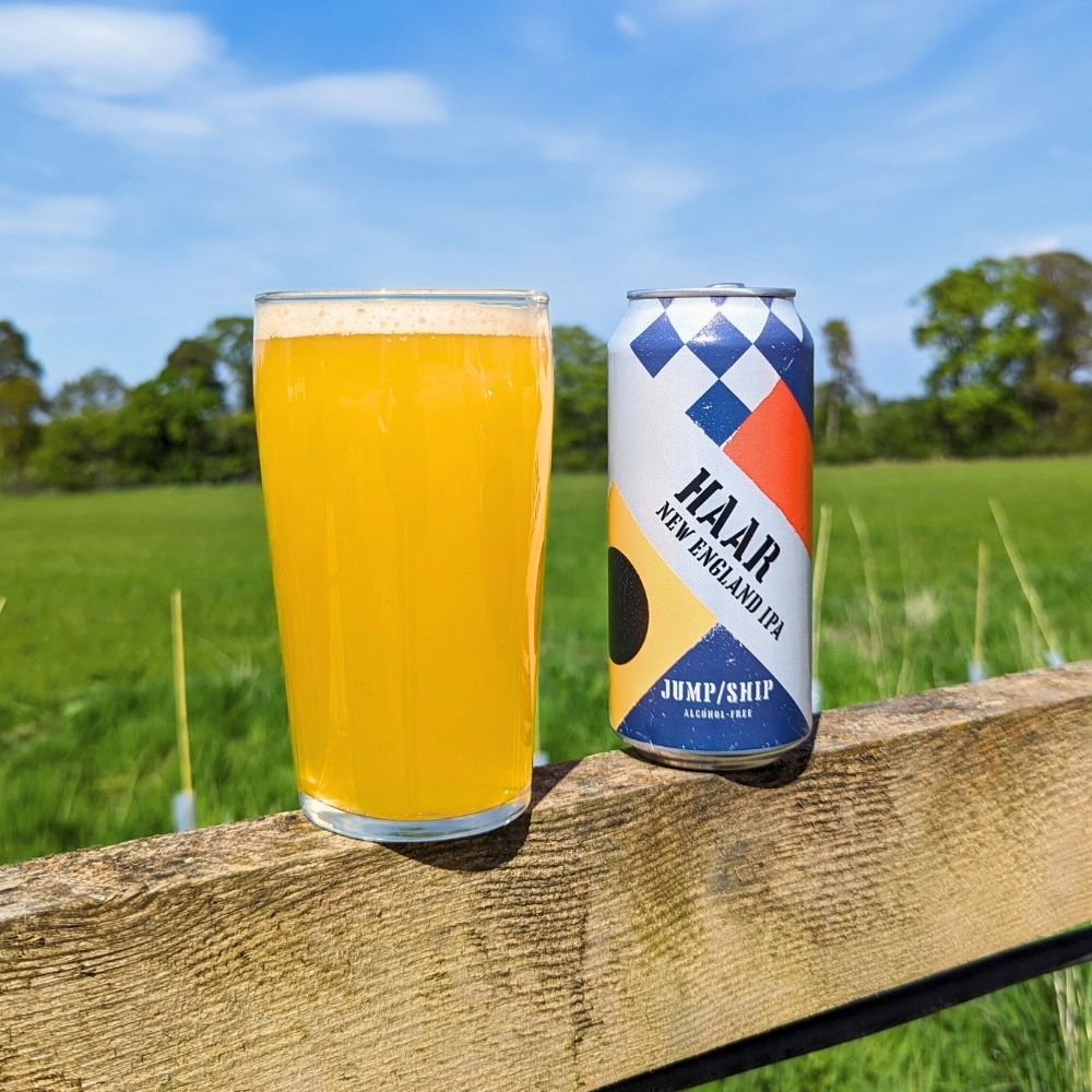 Can of Haar New England IPA and glass on a wooden fence with a field and trees in the background