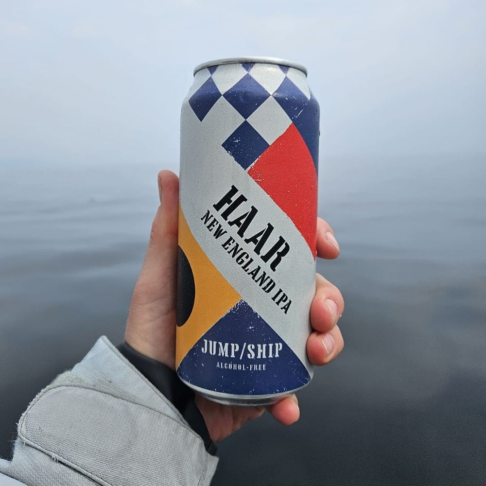 Hand holding a can of 'HAAR New England IPA' against a blurred water background.