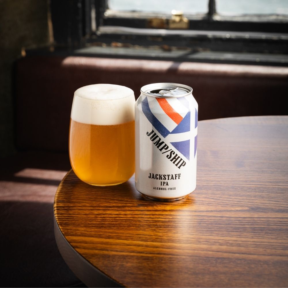 Can of Jackstaff IPA and glass of beer on a wooden table with a window in the background
