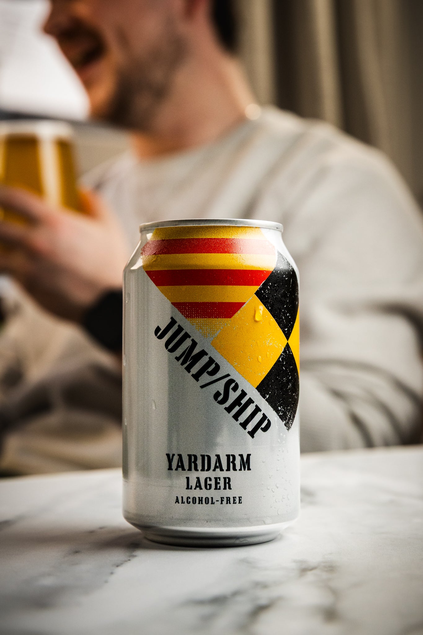 Can of Yardarm alcohol free Lager with a person holding a glass in the background