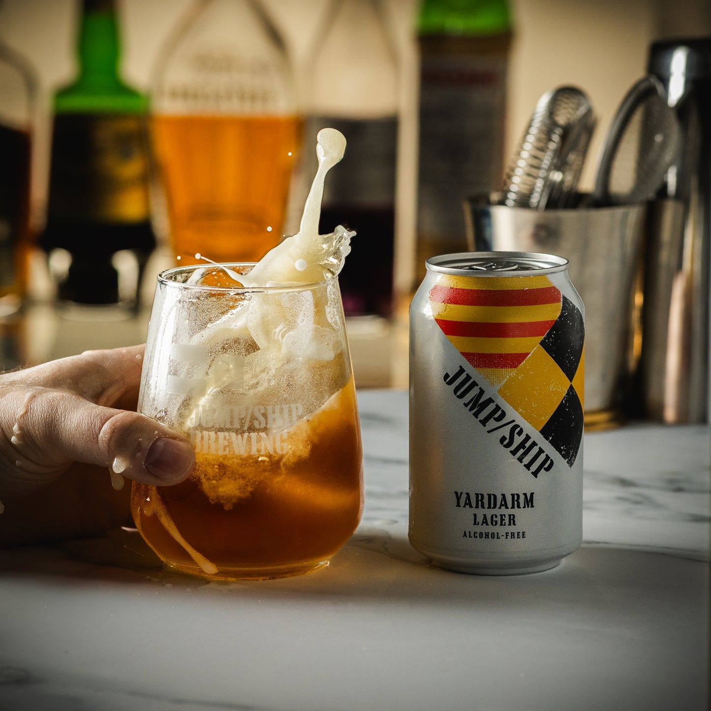 Glass of alcohol free Yardarm lager being placed on a bar next to a can.