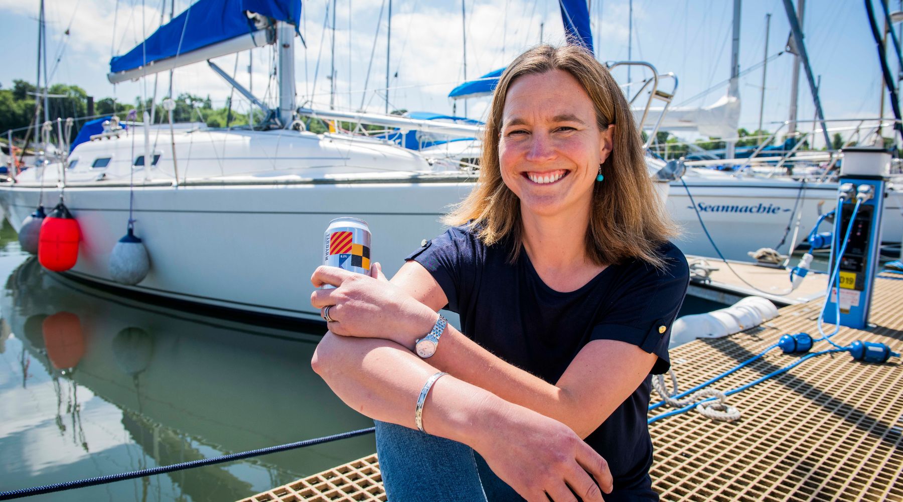 Sonja Mitchell holding a can of the original Jump Ship Yardarm Lager in a marina setting