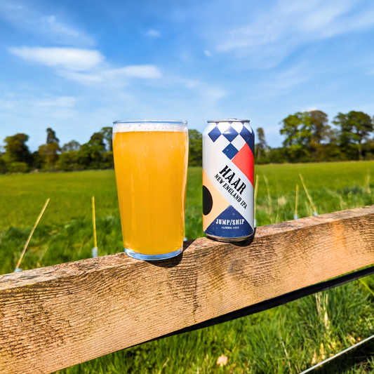 A pint of Haar alcohol free New England IPA on a fence next to a can