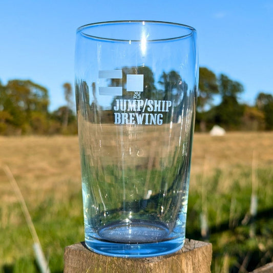 Clear glass with 'Jump/Ship Brewing' text on a wooden post against a natural background