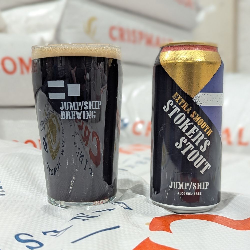 Glass pint and can of Jump/Ship Brewing Stokers Extra Smooth Stout on a pile of malt sacks