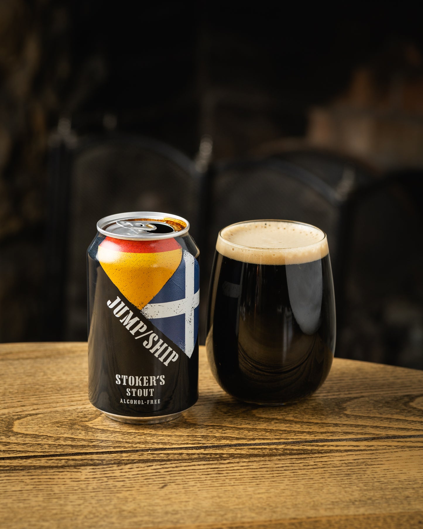 Stoker's stout alcohol-free beer can and glass front side on table in front of fire heart