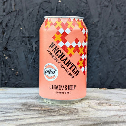 Pink can of 'Uncharted' raspberry & vanilla sour with checkered design on a wooden surface.